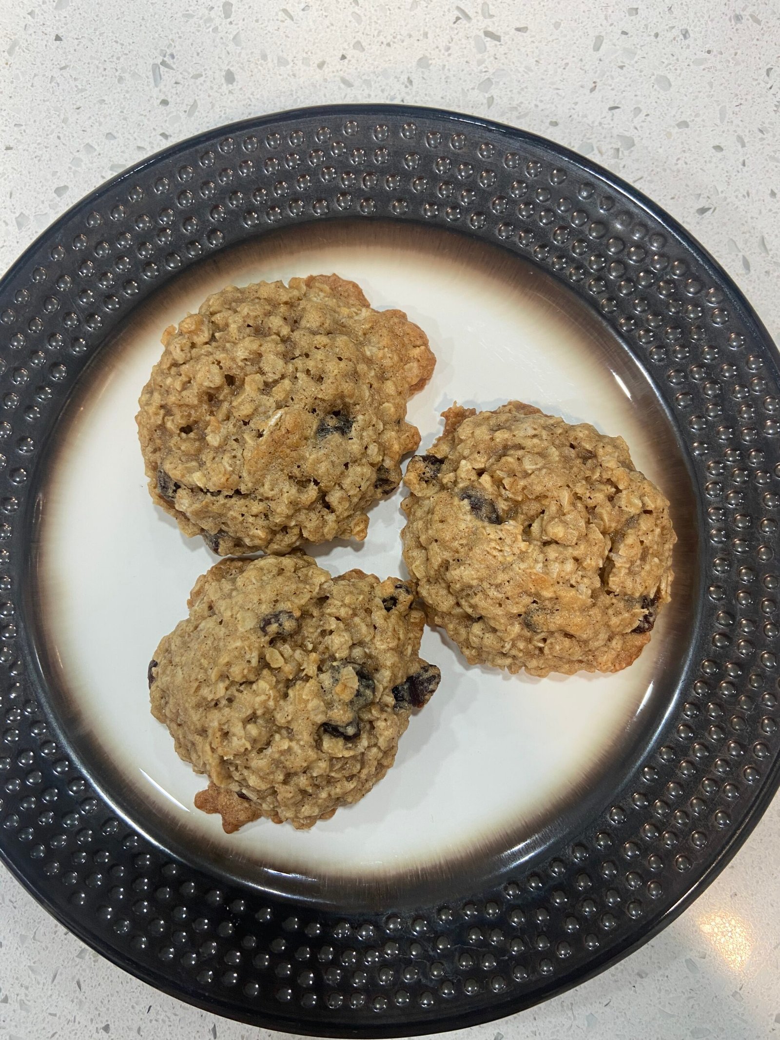 Overhead view of three homemade oatmeal raisin cookies made with quick oats, highlighting their rustic chape and oat-filled texture. 