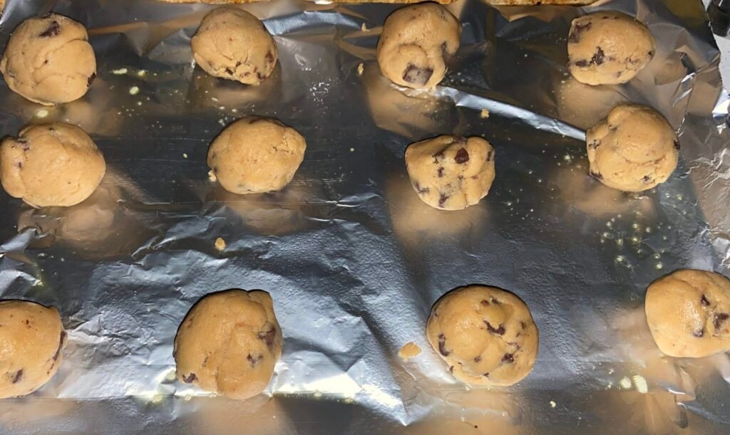 Chocolate chunk cookie dough balls arranged in a baking sheet before baking. 
