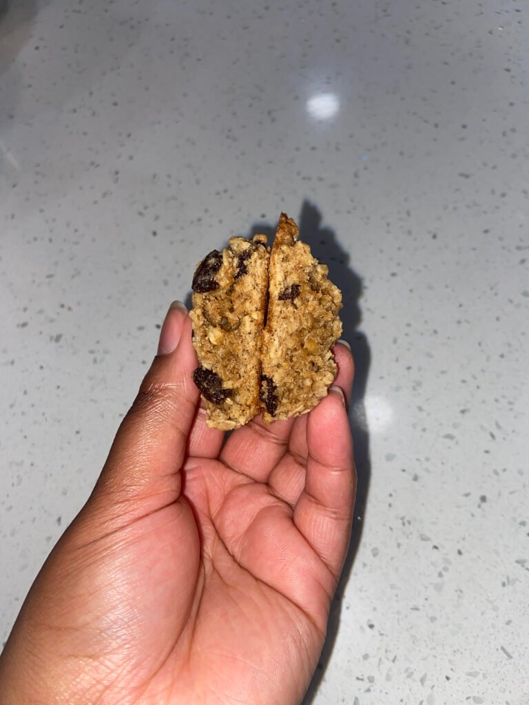A soft baked oatmeal raisin cookie broken in half, showing a chewy center packed with oats, raisins and cinnamon. 